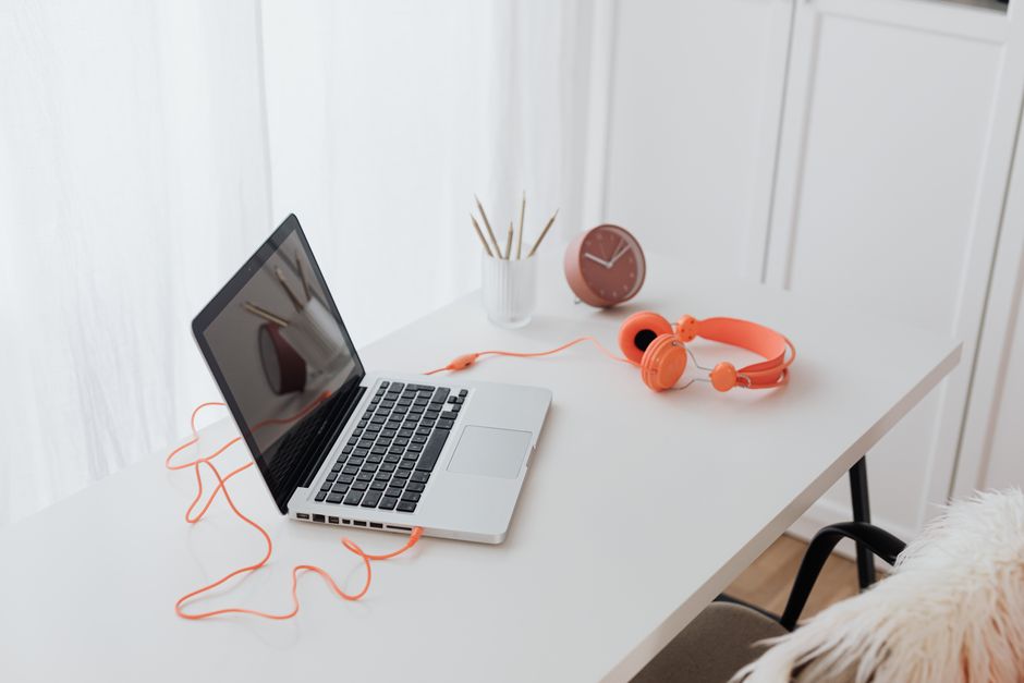 Minimalist workspace featuring a laptop and orange headphones on a clean white desk.