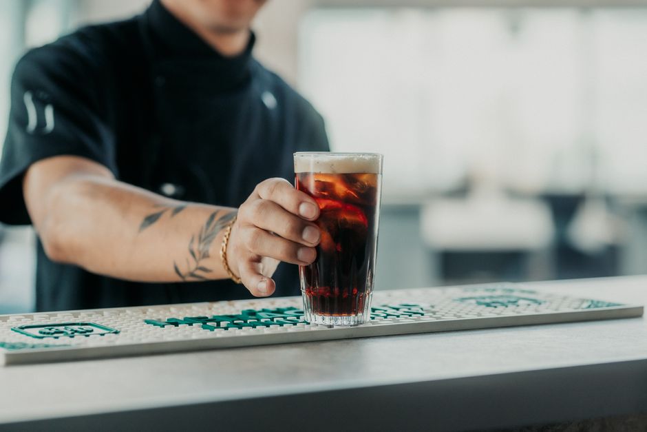 A bartender with tattoos serves a glass of fernet and cola in Buenos Aires.