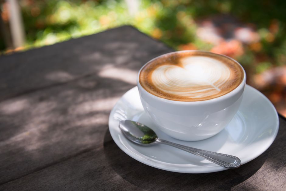 A beautifully crafted latte with heart art on a wooden table outdoors.