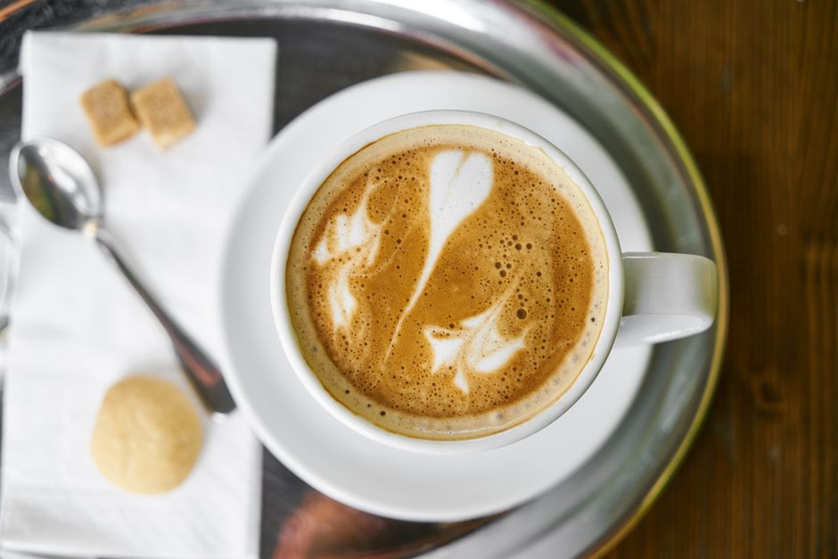 Top view of a cappuccino with intricate latte art, served on a tray with sugar cubes and a cookie.