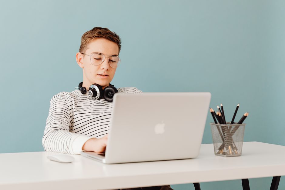 Teen male with headphones working on a laptop at a table, showcasing a focus on technology.