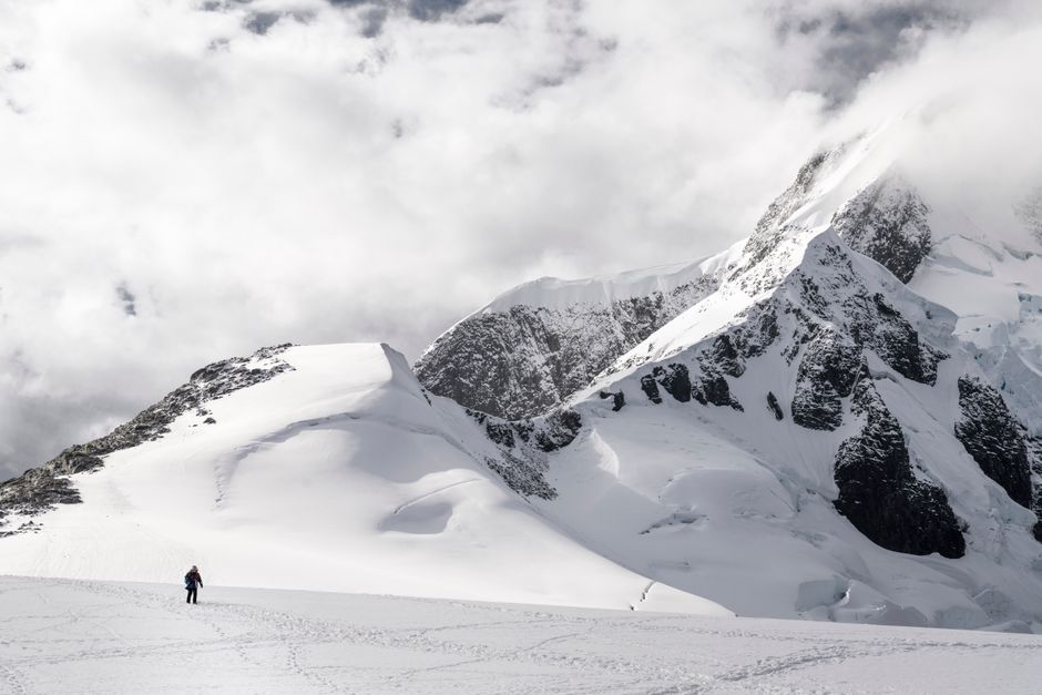 A lone climber traverses a snowy mountain under dramatic clouds.