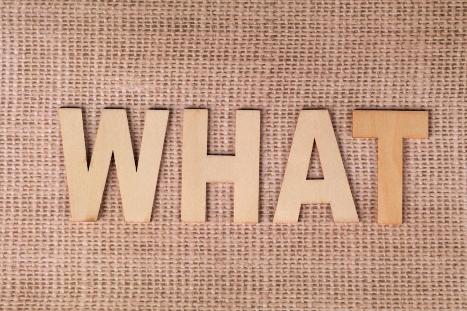 Wooden letters forming the word WHAT set on a textured burlap surface.